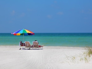 Ein Strand mit einem bunten Sonnenschirm und zwei Liegestühlen, die auf den Ozean ausgerichtet sind.