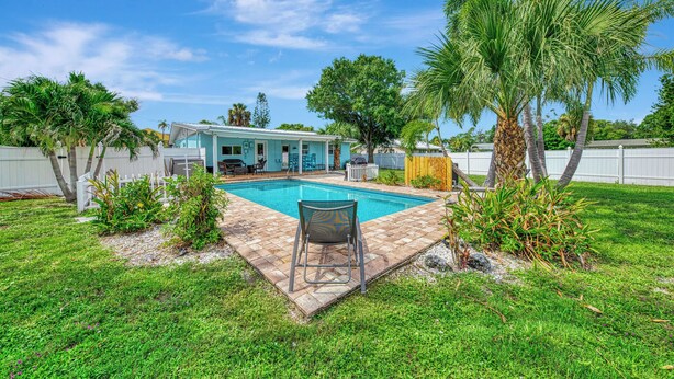 Ein Garten mit Swimmingpool, einer überdachten Terrasse und einem Haus mit blauer Fassade.