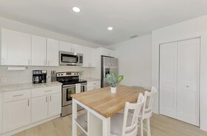 A modern kitchen with white cabinets, stainless steel appliances, and a wooden dining table with chairs. - Private pool, Next to the island and downtown- The best of both worlds (Sarasota)