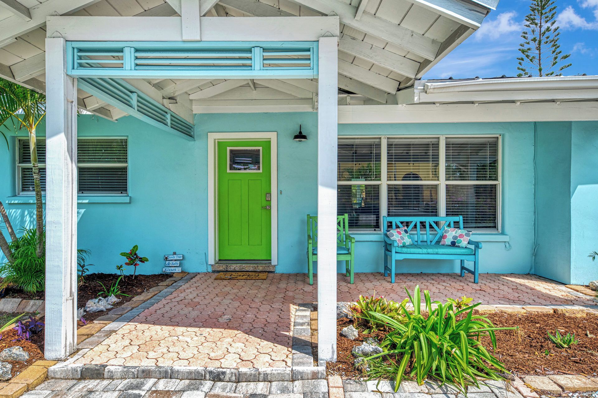 A house with a green door, a porch with a blue bench, and a window with blinds.