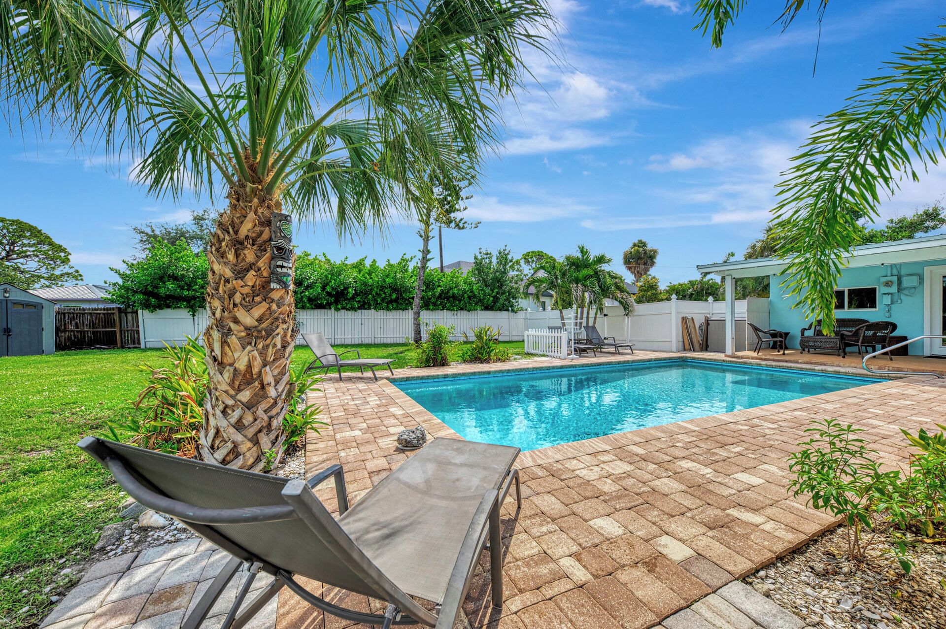 A backyard with a swimming pool, a palm tree, and a covered patio area.