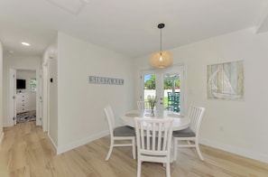 A dining area with a white table, chairs, and a hanging light fixture.