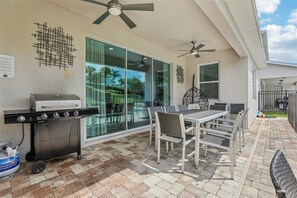 An outdoor patio with a grill, seating, and ceiling fans. - Orlando Home: Private Pool & Themed Rooms (Kissimmee)