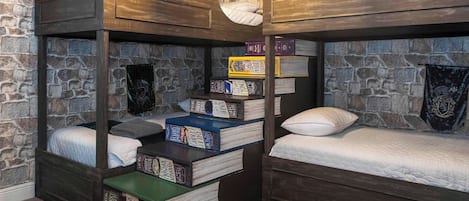A multi-level bunk bed room with stone walls, wooden shelves, and a variety of books.