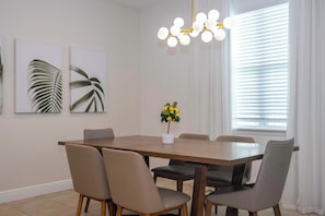 A dining room with a wooden table, six chairs, a chandelier, and two wall-mounted plant prints. - Pool, Spa & Game Room Home for 12 at Encore (Kissimmee)