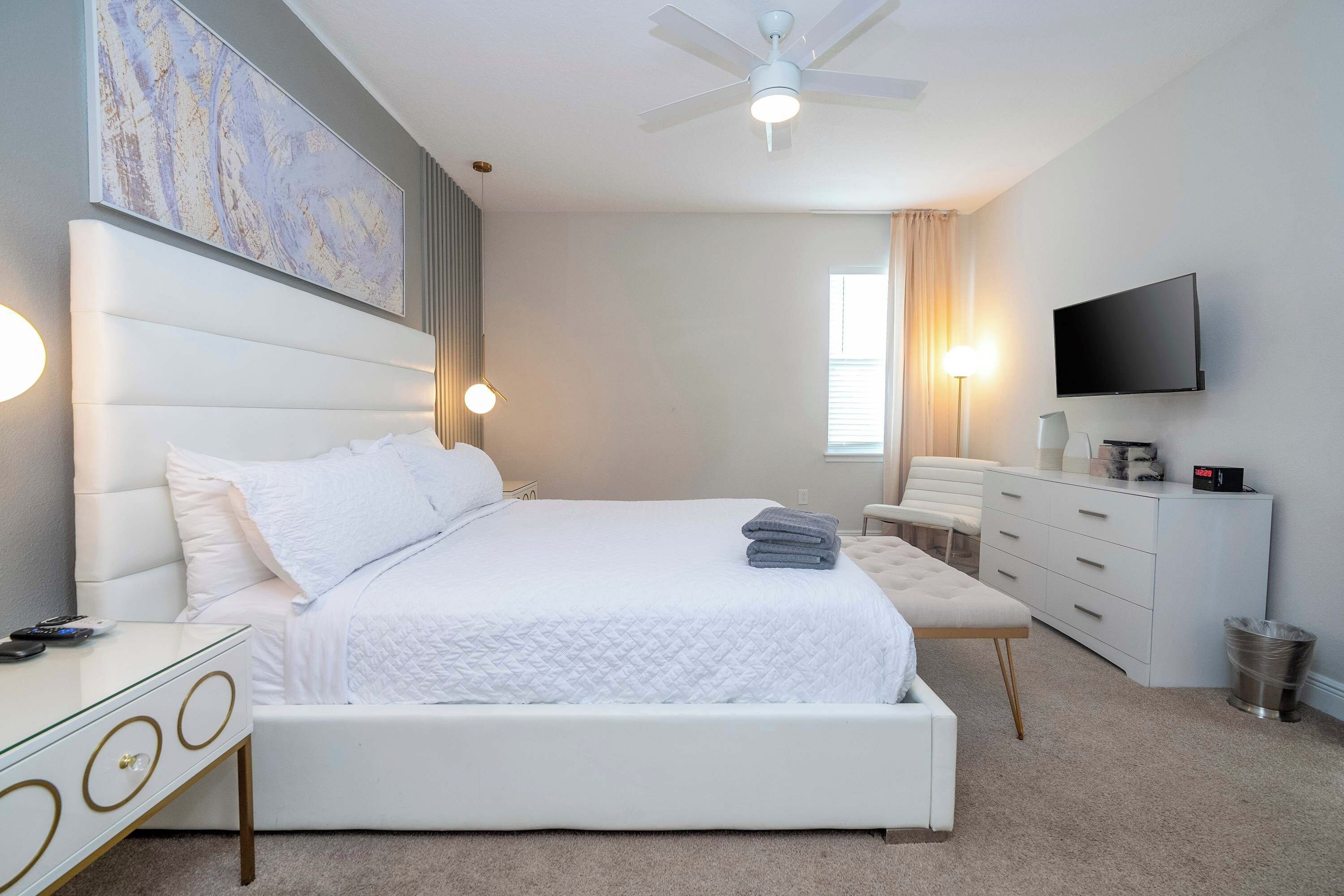 A modern bedroom with a large bed, a flat-screen TV, a bedside table, and a ceiling fan.
