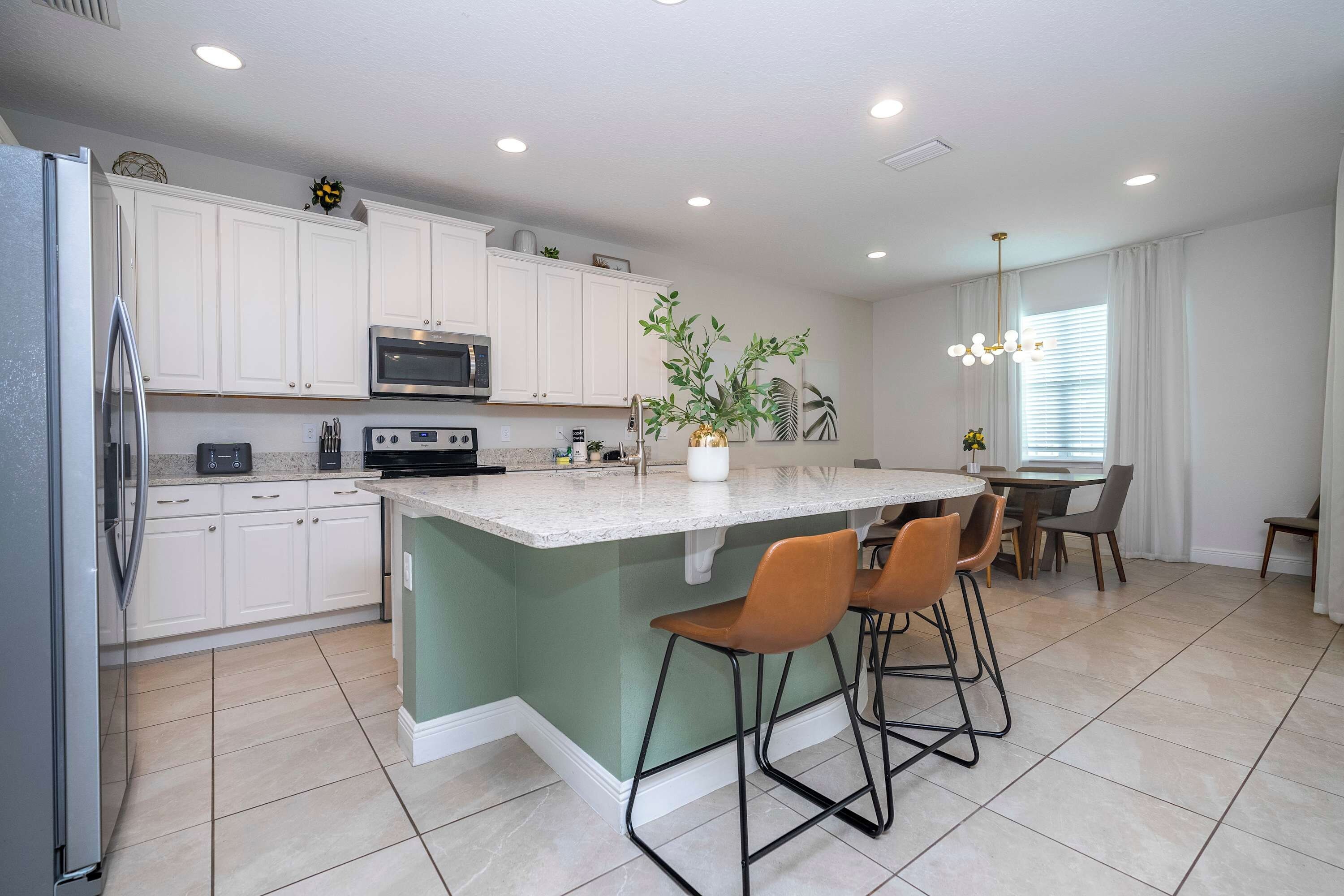 A modern kitchen with white cabinets, a built-in oven, a microwave, and a central island with bar stools.