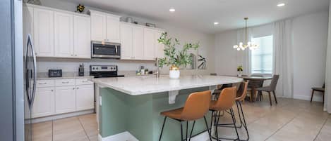 A modern kitchen with white cabinets, a built-in oven, a microwave, and a central island with bar stools.