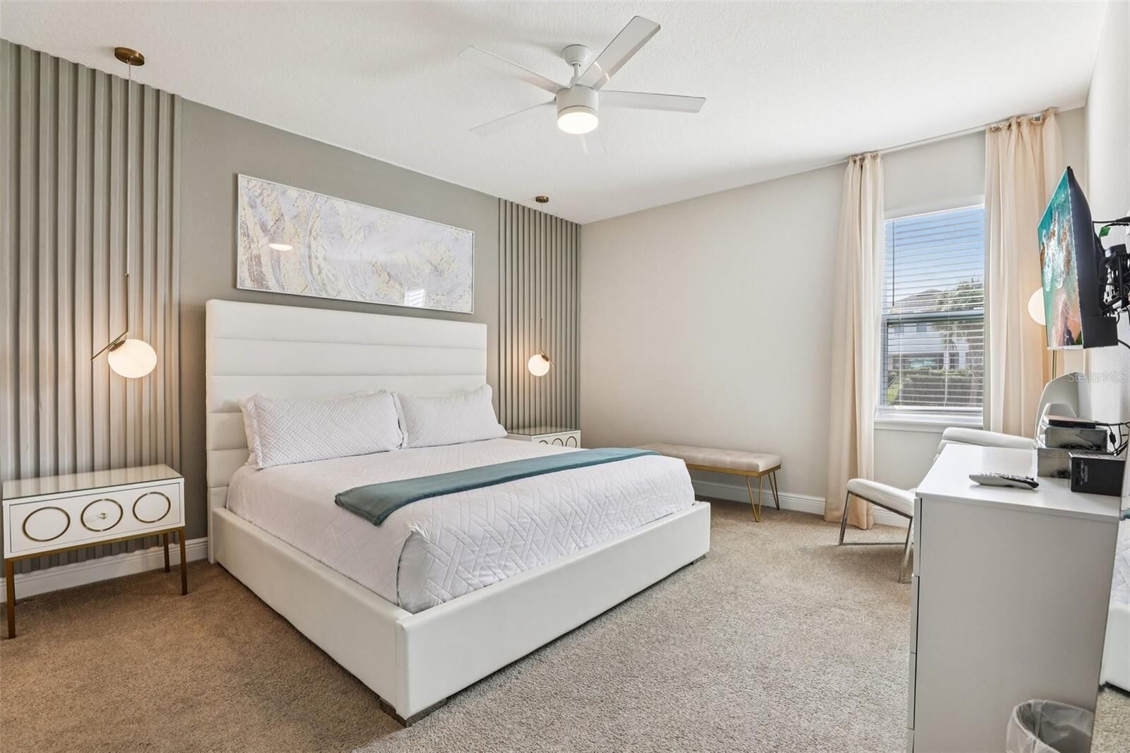 A modern bedroom with a bed, bedside tables, a desk, and a ceiling fan.
