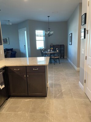 A modern kitchen with a central island, dark cabinetry, and a dining area with a chandelier. - Golf Course-Pond, 2 Bed/2 Bath+ Den 2022 Villa-Quiet Active 55+ Gated Community (Port Charlotte)