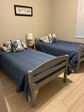 A bedroom with two single beds, a bedside table with a lamp, and a framed picture on the wall. - Golf Course-Pond, 2 Bed/2 Bath+ Den 2022 Villa-Quiet Active 55+ Gated Community (Port Charlotte)