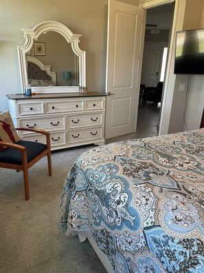 A bedroom with a bed, dresser, chair, and a television. - Golf Course-Pond, 2 Bed/2 Bath+ Den 2022 Villa-Quiet Active 55+ Gated Community (Port Charlotte)
