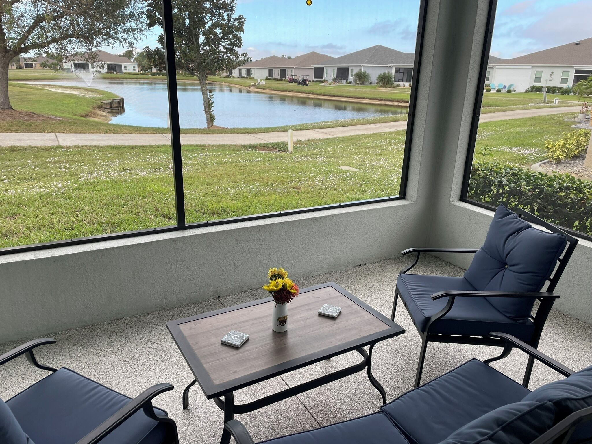A room with a view of a lake, a table with a vase, and two chairs.