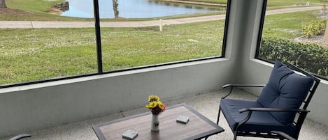 A room with a view of a lake, a table with a vase, and two chairs.