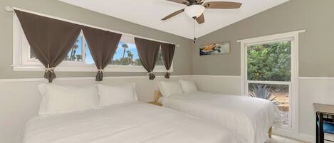 A bedroom with two beds, a ceiling fan, and a window with curtains.