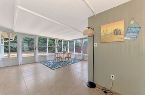 Ein geräumiges Zimmer mit großen Fenstern, einer Essecke mit Stühlen und Tisch, einem gemusterten Teppich und Kunstwerken an der Wand.