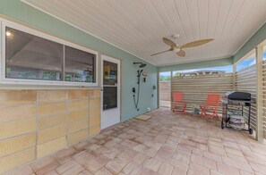 Ein überdachter Patio-Bereich mit Deckenventilator, Grill und zwei roten Stühlen.