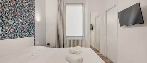 Habitación de hotel con cama, televisor, ventana con cortinas y pared estampada.
