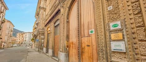 A building with large wooden doors and a sign indicating 'L'Opera' and 'Rooms.'
