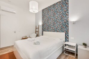 A modern bedroom with a large bed, a bedside table, a wall-mounted air conditioner, and a patterned wallpaper. - [Rooms Camera2] 5Terre-Near the station+A/C (La Spezia)