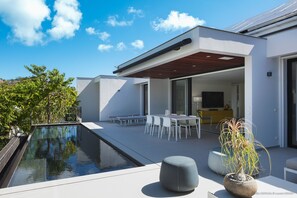 A modern outdoor patio with a pool, seating area, and a dining table.