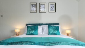 A bed with a teal and white bedspread, two white pillows, and a teal headboard. There are two bedside lamps on either side of the bed. Above the bed, there are three framed artworks on the wall. - The Waltons – Ideal Durham Escape - Nature Lovers - Pass the Keys (New Brancepeth)