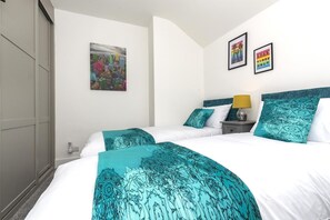 Een hotelkamer met een bed, een nachtkastje, een lamp en twee ingelijste foto’s aan de muur.