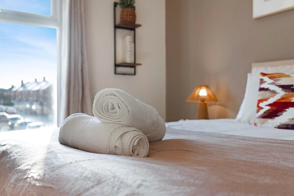A neatly made bed with rolled white towels, a bedside lamp, and a view of the street through a window. - Characterful 3 Bed | Sleeps 6 | Central Darlington - Pass the Keys (Darlington)
