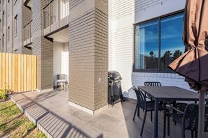 Eine Terrasse mit Grill, Sitzgelegenheit im Freien und Blick auf ein Wohngebäude.