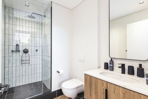 Ein modernes Badezimmer mit Duschkabine aus Glas, einer weißen Toilette und einem Waschtisch mit Spiegel und Pflegeprodukten.
