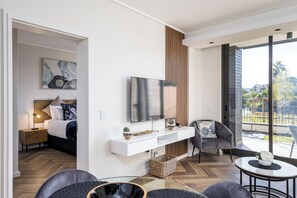 Ein modernes Hotelzimmer mit Bett, Fernseher, einer Sitzecke mit Stuhl und kleinem Tisch sowie einem Balkon mit Blick.