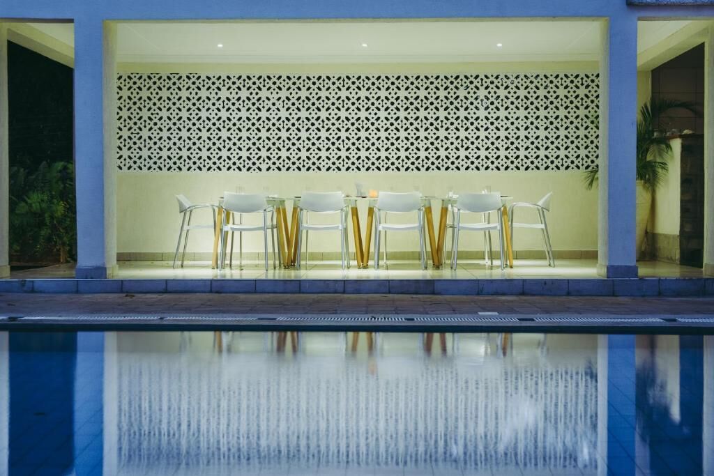 Zona de piscina con mesa y sillas, un muro decorativo y una piscina cristalina.