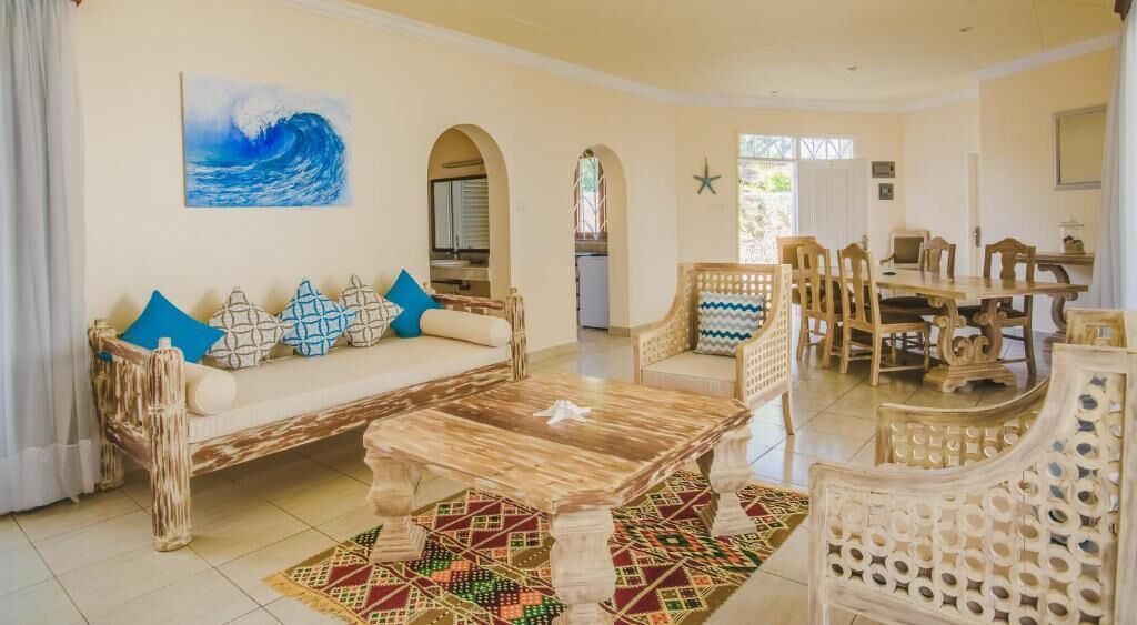 Una sala de estar con sofá, mesa de centro y sillas, un comedor con mesa y sillas, y una cocina al fondo.