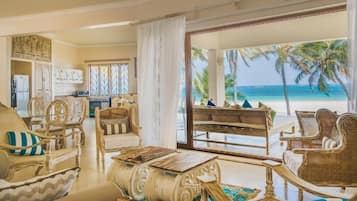 A spacious living area with a view of the beach, a dining table, and wicker furniture.