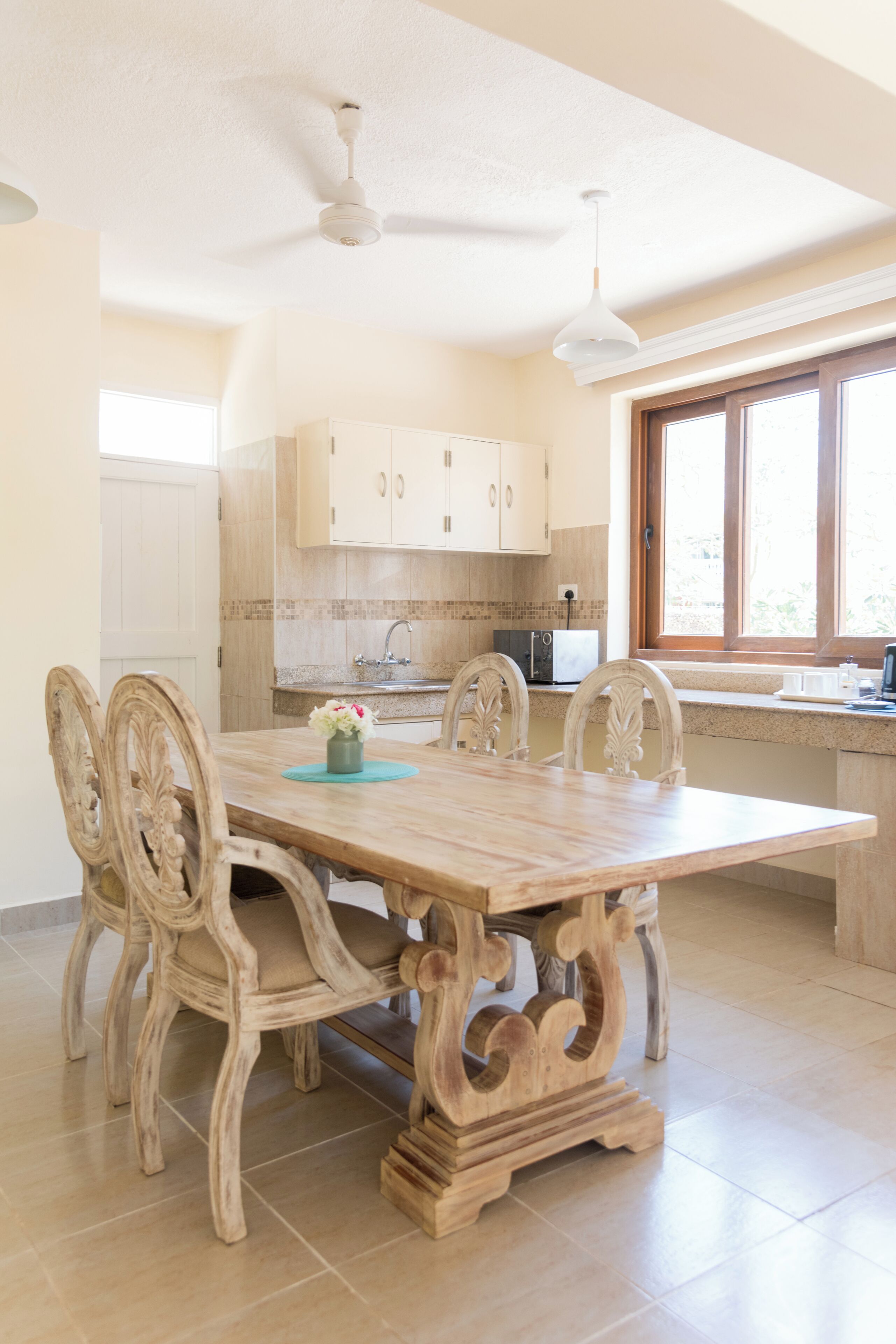 A dining area with a wooden table and chairs, a ceiling fan, and a window with a view.