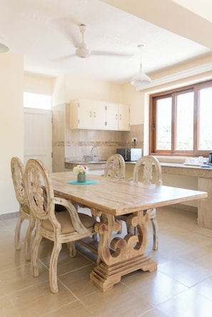 A dining area with a wooden table and chairs, a ceiling fan, and a window with a view. - The Zubeida (Diani Beach)