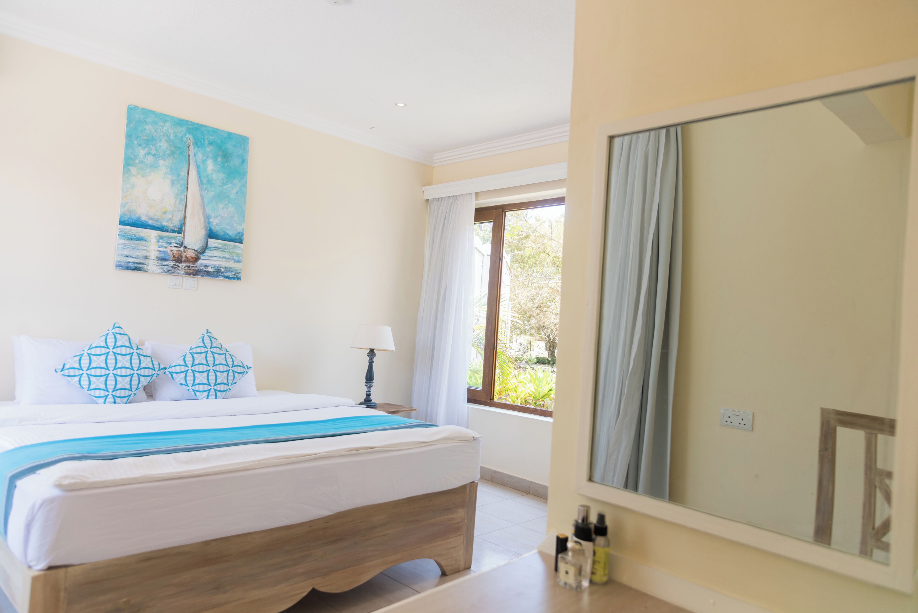 Habitación de hotel con una cama, un cuadro de un velero, una ventana con cortinas y un espejo grande.