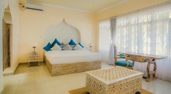 Une chambre d’hôtel avec un grand lit, une petite table, une tête de lit décorative et une fenêtre avec des rideaux.