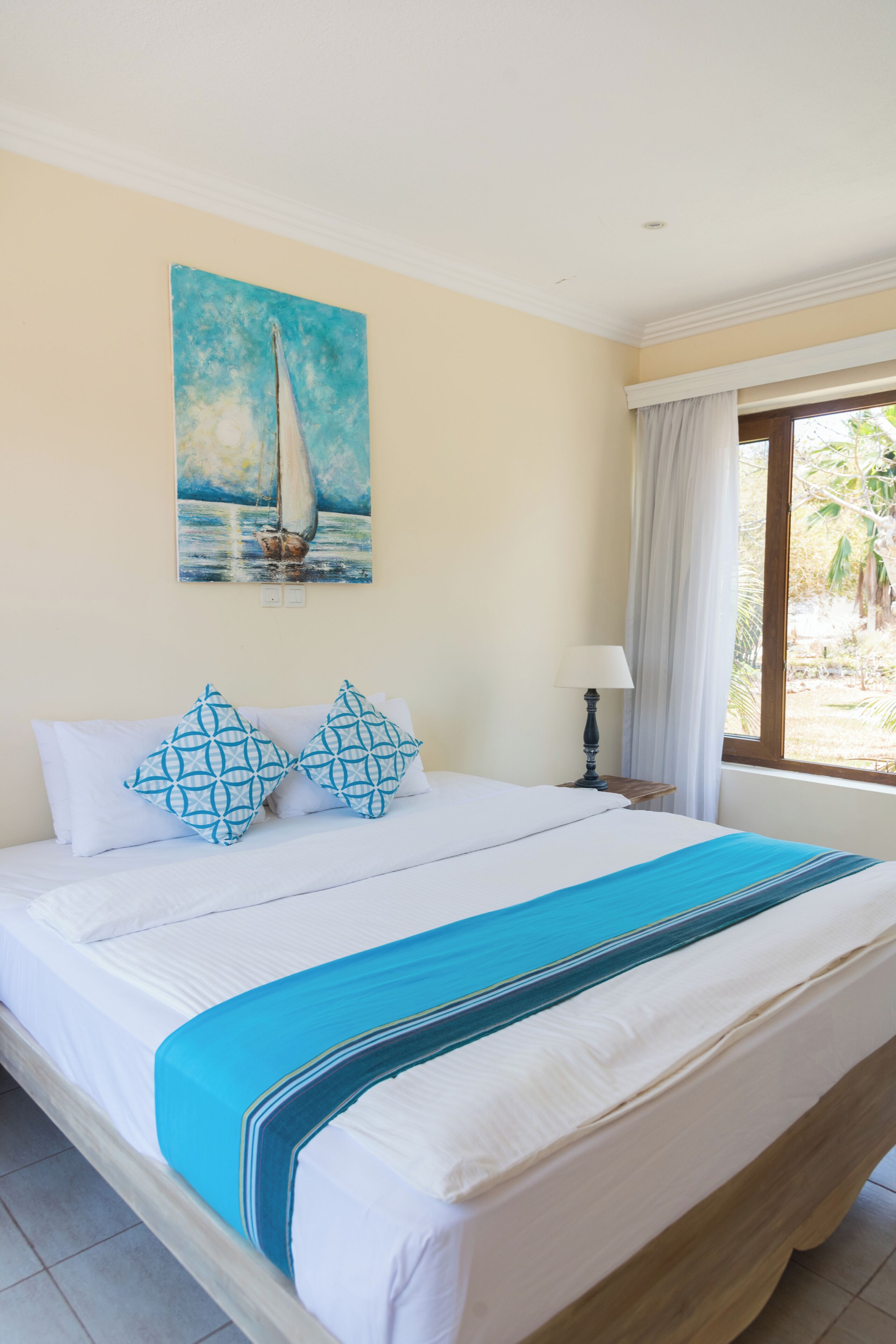 Una habitación de hotel con una cama, un cuadro de un velero y una ventana con cortinas.