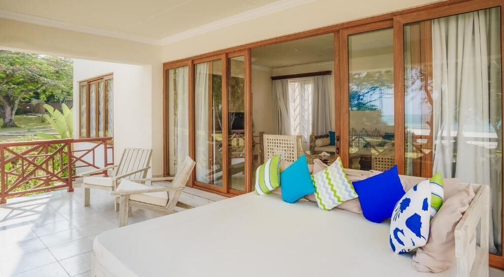 Una habitación con cama, dos sillas, una mesa y un ventanal corredizo que da a un balcón.