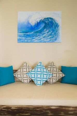 A room with a beige sofa, patterned cushions, and a painting of a wave.