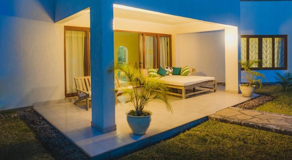 A modern outdoor seating area with a table and chairs, a potted plant, and a glass door leading to a room.