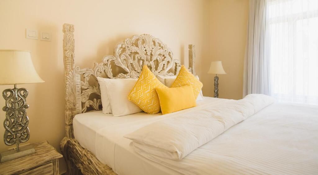 A neatly made bed with white linens and decorative pillows, a carved headboard, and bedside lamps on either side.