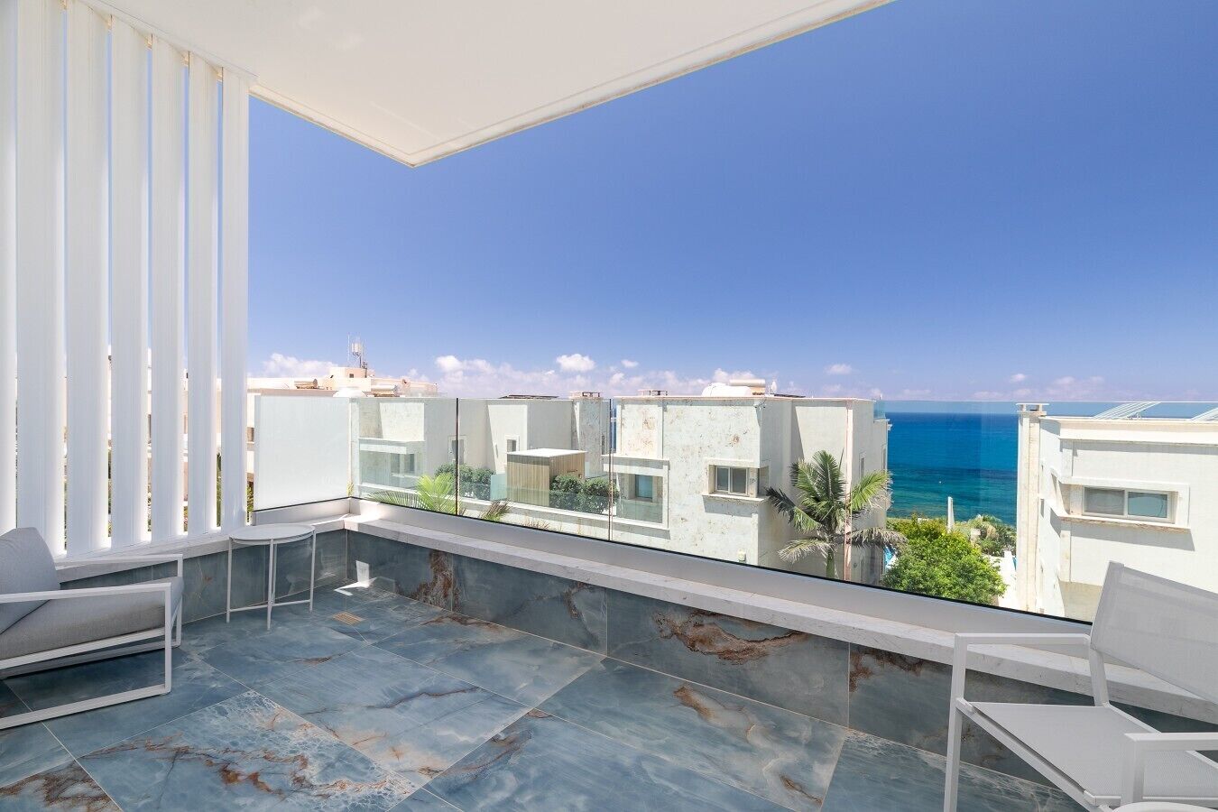 A balcony with a view of the sea, white furniture, and a tiled floor.
