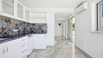 Una cucina moderna con mobili bianchi, uno schienale decorato e un pavimento in marmo.