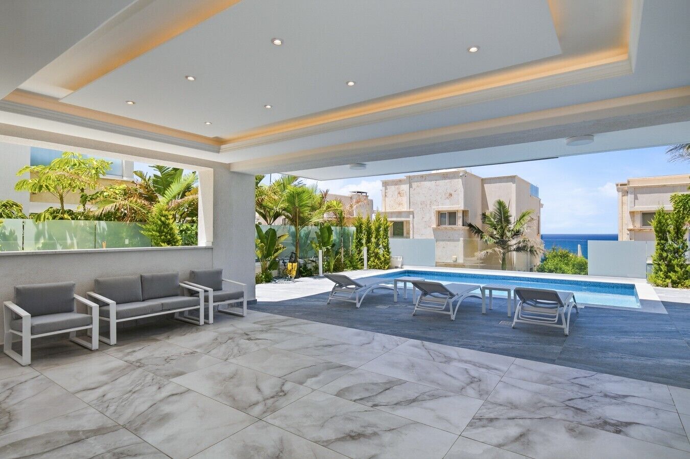 A modern outdoor living area with a pool, seating, and a view of the sea.