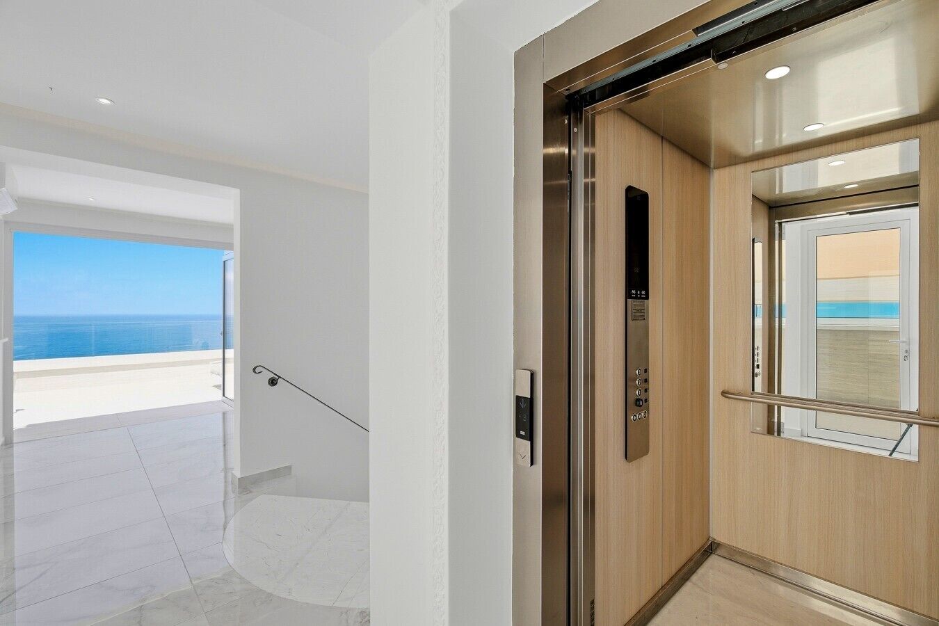 Un ascensore moderno con pannello di controllo, porta in vetro e vista sull'oceano attraverso il balcone adiacente.
