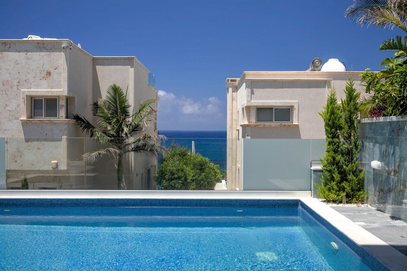 Una piscina con vista sull'oceano, circondata da edifici con balconi e un po' di vegetazione.