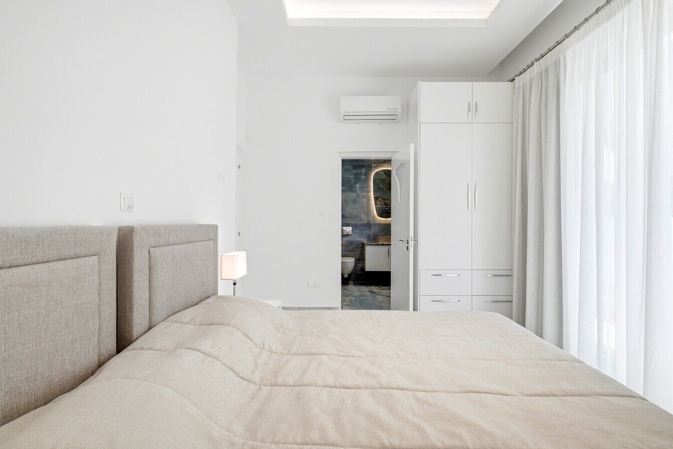 A modern hotel room with a large bed, a wardrobe, and a bathroom visible through an open door.