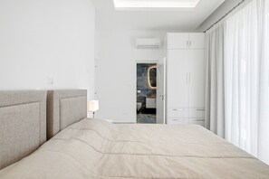 Ein modernes Hotelzimmer mit einem großen Bett, einem Kleiderschrank und einem durchgegangenen Tür geöffnet sichtbarem Badezimmer.